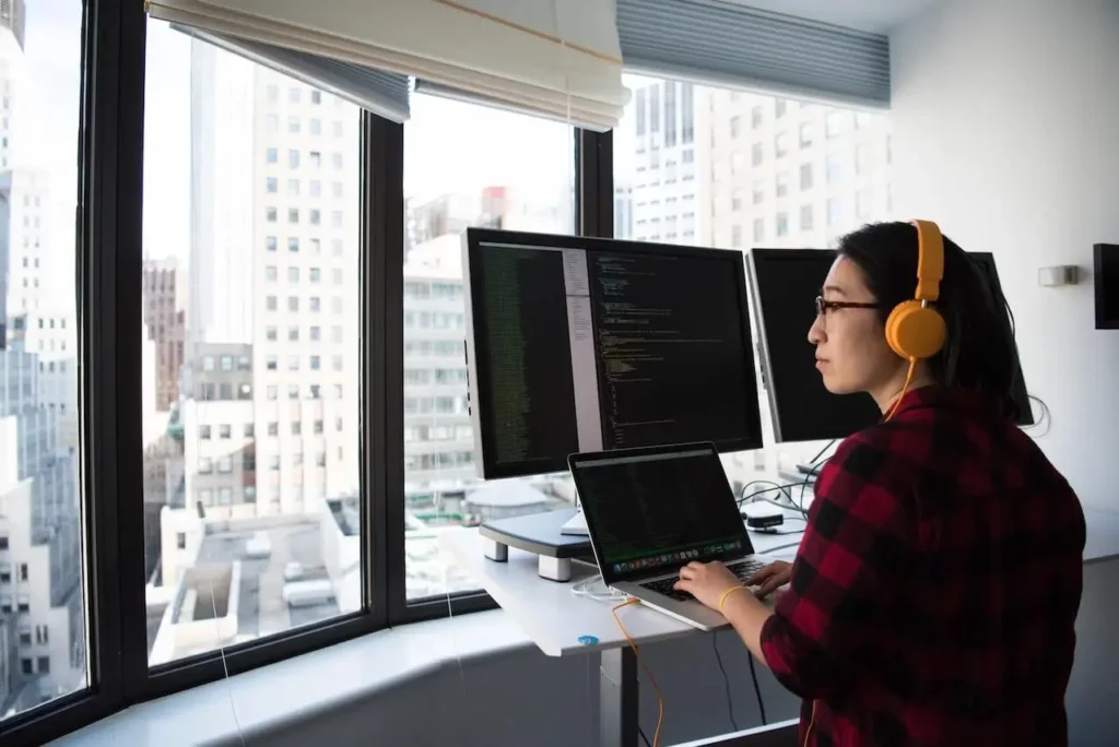 Cette image représente une femme de dos qui travail sur un ordinateur avec du code sur l'écran, elle sert à contribuer à l'article de blog sur le WMS sur le site CPGI.