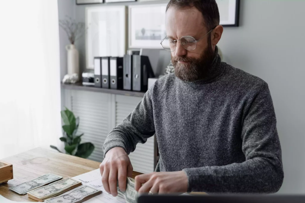 Image d'un homme assis entrain de compter des liasses de billets dans un bureau