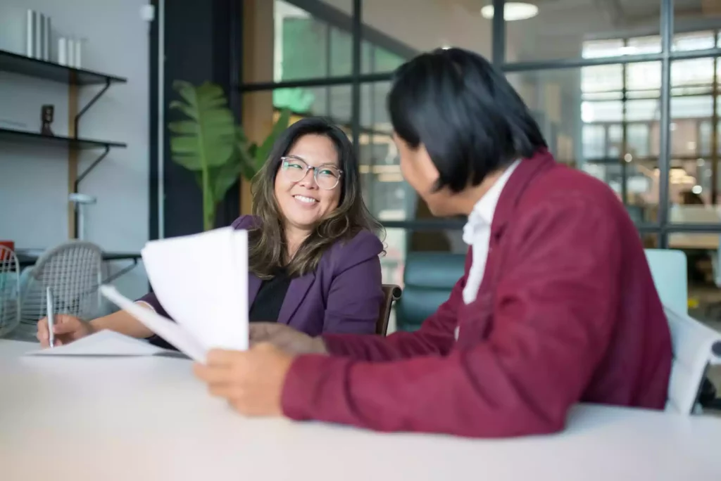 Deux collègues discutant de documents à une table dans un bureau moderne.