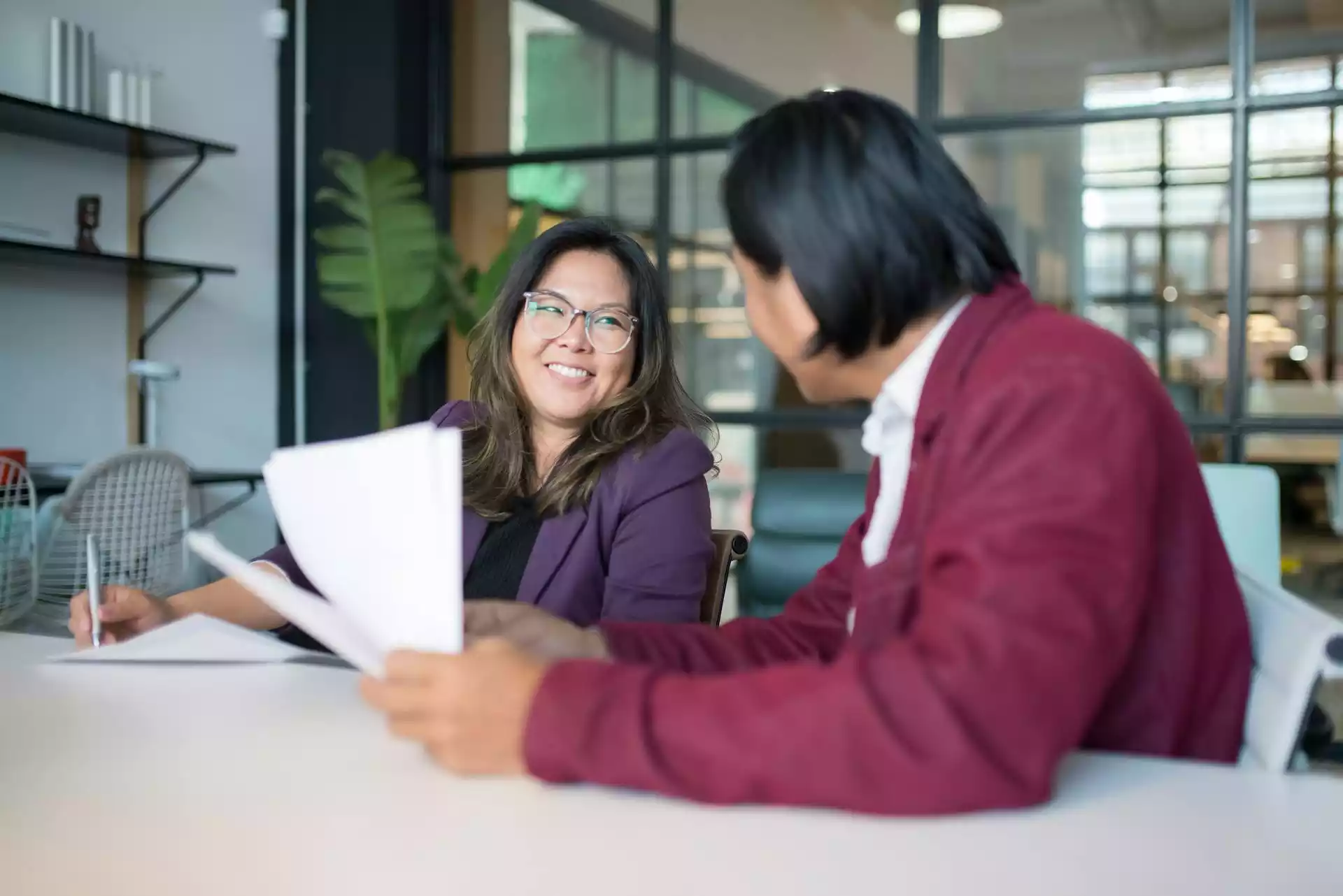 Deux collègues discutant de documents à une table dans un bureau moderne.