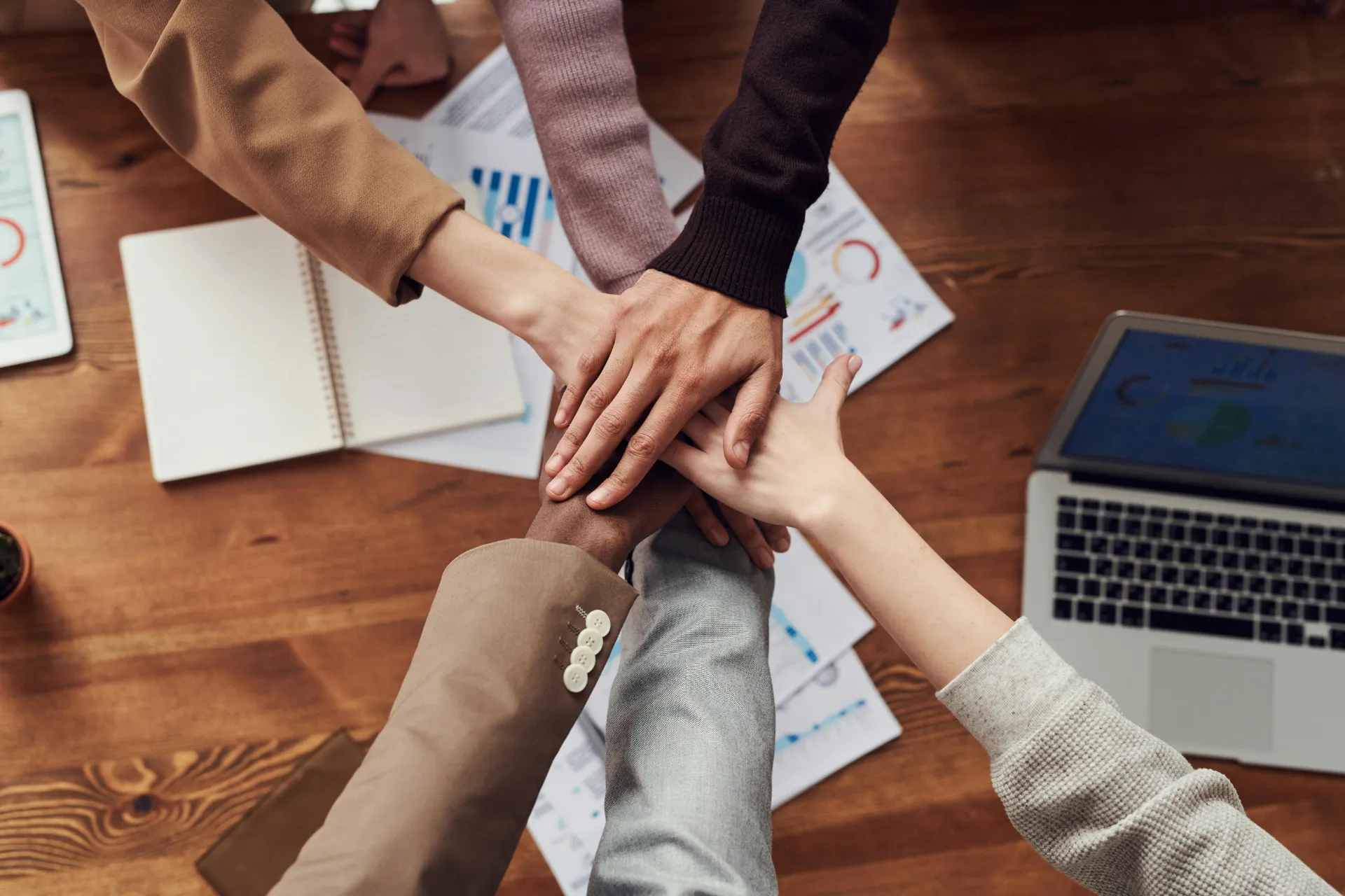 Mains de plusieurs personnes se superposant sur un bureau de travail, symbolisant l'esprit d'équipe.