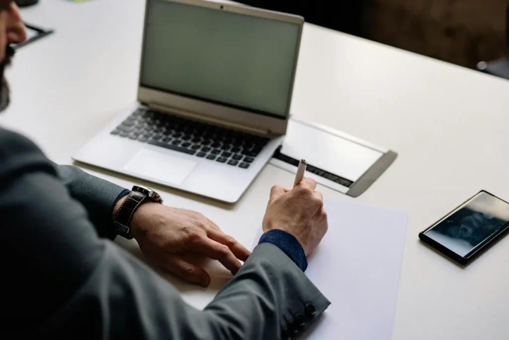 bureau avec les bras d'un homme entrain d'écrire et un ordinateur portable